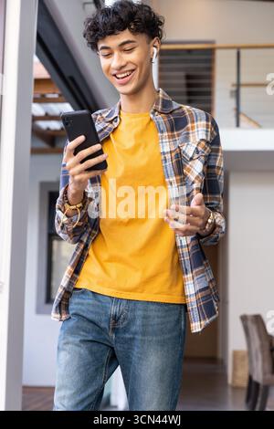 Man smiling while checking smartphone and gesturing in home wearing wireless earbuds Stock Photo
