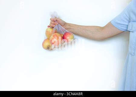 Woman holding fresh red apples in transparent mesh produce bag. Zero waste grocery shopping, plastic-free lifestyle, reusable packaging alternatives Stock Photo