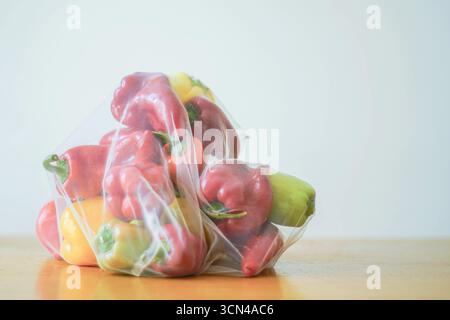 A kilogram of fresh green, yellow, and red bell peppers, packed in a reusable mesh bag on a wooden table against a light wall. Farm-to-table concept Stock Photo
