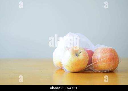 Golden apples packaged in mesh produce bag on wooden surface. Fruits in eco-packaging. Concept of harm-to-table, organic farming, plastic-free storage Stock Photo