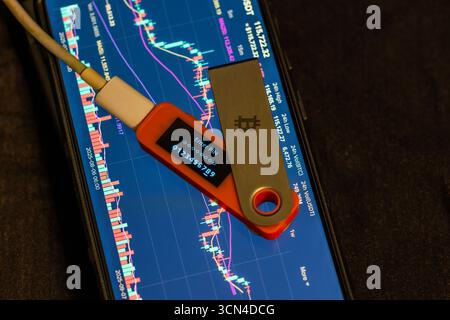Close-up view of hardware security key showcasing enter PIN code message over smartphone displaying cryptocurrency market data. Stock Photo