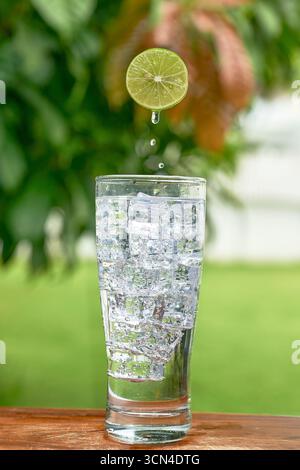 A high-speed photograph of a lime droplet falling into a cold glass of soda water. A dynamic and refreshing concept for summer, hydration, and healthy Stock Photo