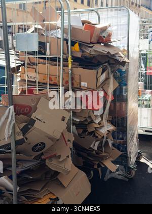 Versailles, France - 18 September 2025: A large quantity of used cardboard packaging is piled high in metal roll cages outside a grocery store. This vertical image shows post-delivery waste. Stock Photo