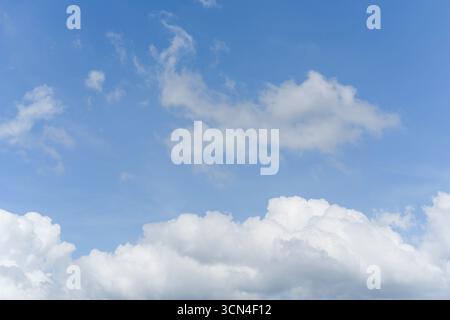 White fluffy clouds float gently in a clear blue sky on a bright sunny day. The scene feels open clean and refreshing. Stock Photo
