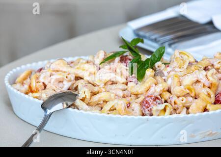 Creamy pasta salad with shrimp and cherry tomatoes, garnished with fresh basil, served in an elegant white dish, perfect for a summer meal or party Stock Photo