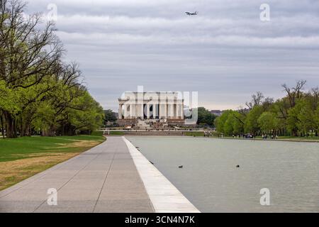 An airplane flies over the Lincoln memorial and reflecting pool in DC Stock Photo