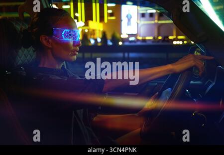 Woman in Futuristic High-tech VR Eyewear driving car in night ci Stock Photo