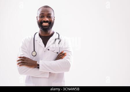A cheerful black doctor stands with arms crossed, smiling confidently in a studio setting, symbolizing medical expertise and success. Stock Photo