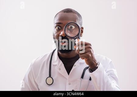 Portrait of shocked African American doctor who is looking through magnifying glass. Stock Photo