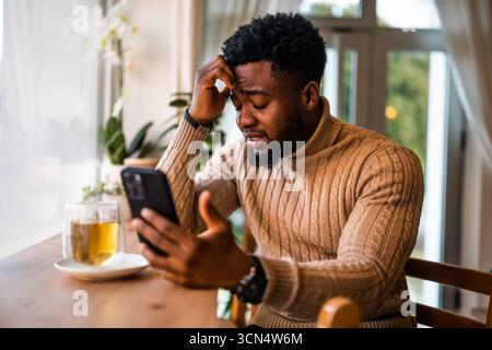 Young black man sitting in bar. He is freelancer on job pause, tired and exhausted. Stock Photo