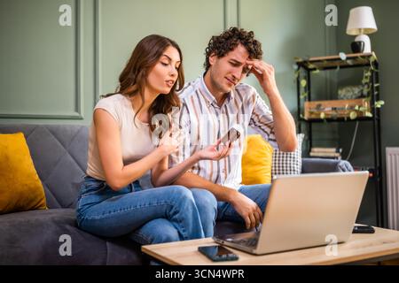 Adult couple sitting on bed in living room and having online doctor's appointment using laptop. Man having headache. Remote consulting with doctor. Stock Photo