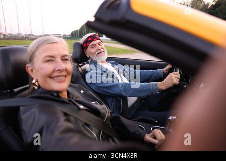 Senior woman taking selfie while man driving cabriolet outdoors, selective focus Stock Photo