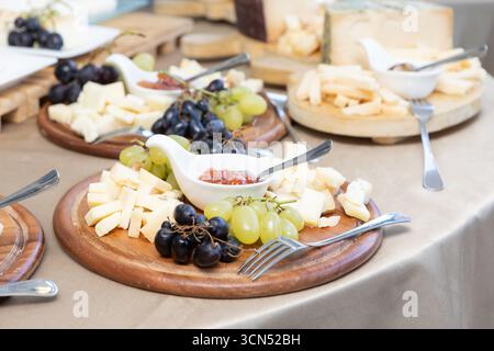 Wooden cheese boards presenting an assortment of cheeses, grapes, and jam, creating an elegant catering display Stock Photo