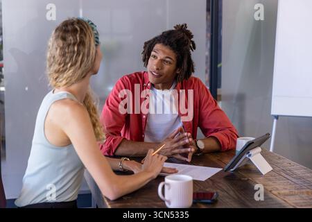 Diverse colleagues discussing documents in meeting room using pencil and tablet with coffee mugs Stock Photo