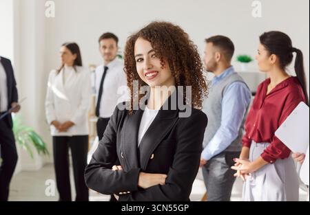 Portrait Of A Happy Curly-Haired Businesswoman With Team In Office Stock Photo