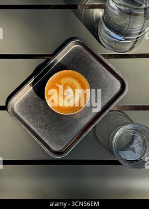 A rich, decaffeinated coffee with plant-based milk, featuring delicate latte art, is presented on a minimalist tray. The pastel colors and warm lighting evoke a serene autumn atmosphere. Stock Photo