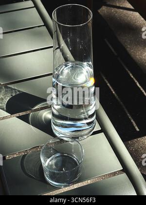 A tall, slender glass carafe filled with water stands on a cafe table. A smaller glass sits next to it, ready to be filled, highlighting a simple and refreshing moment. Stock Photo