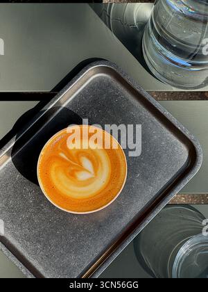 A small cup of coffee with a perfect heart in the foam sits on a metal tray. This image emphasizes the availability of plant-based milks and a sustainable, vegan-friendly lifestyle. Stock Photo