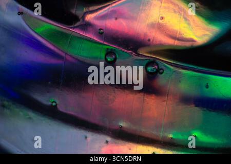 Abstract macro photo of colorful liquid bubbles on a textured surface, showing vivid reflections in purple, blue, yellow, green, and red with light di Stock Photo