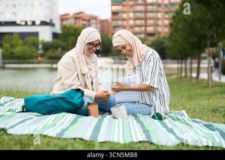 Muslim women students studying outdoors laughing together Stock Photo