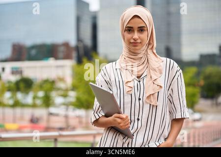 Young muslim woman student holding laptop outdoors Stock Photo
