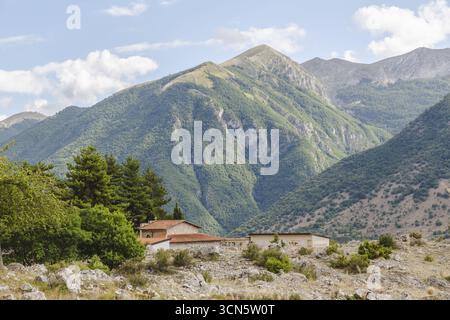 View of sun-drenched buildings nestle at the foot of a majestic mountain range, verdant slopes contrasting with the rocky foreground, Frattura Vecchia, Abruzzo, Italy. Stock Photo