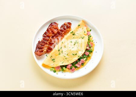 Stuffed omelette with ham and green onion served with crispy fried bacon on plate on light background. Close up view Stock Photo
