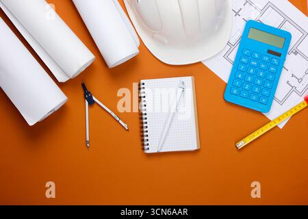 Engineering construction safety helmet, blueprint rolls, project plan and calculator on brown background. Calculation of the cost building a house. To Stock Photo