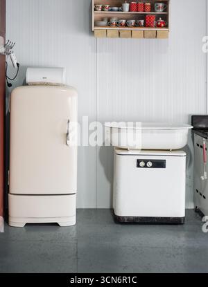 Mid-20th-century kitchen interior. Vintage rounded-shaped refrigerator, vintage wringer washing machine; shelves with polka dot jars above on the wall Stock Photo
