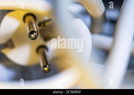 Close-up of a white power plug, Schuko plug, focus on the contact pins with blurred power cable in the foreground and background and with yellow light Stock Photo