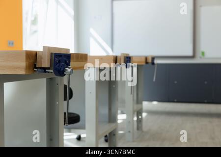 Well-lit workshop features several wooden workbenches, ready for projects in a modern classroom. Stock Photo