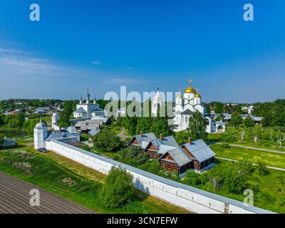 An aerial view of the Pokrovsky Monastery with its white buildings and golden domes, with traditional wooden houses in the foreground. Stock Photo