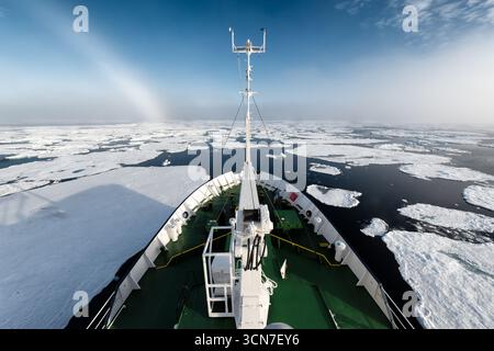 Ship Deck Navigating Arctic Ice Floes Svalbard Norway / SVALBARD, Svalbard and Jan Mayen — A ship navigates through scattered ice floes in the Arctic Ocean near the Sjuøyane archipelago, the bow cutting through dark water amid a wide expanse of broken ice. Svalbard sits roughly midway between mainland Norway and the North Pole, and the waters north of Nordaustlandet around Sjuøyane are among the most ice-affected in the archipelago. The entire Sjuøyane group is protected within the Nordaust-Svalbard Nature Reserve, established on 1 July 1973, making access tightly regulated and expedition vess Stock Photo