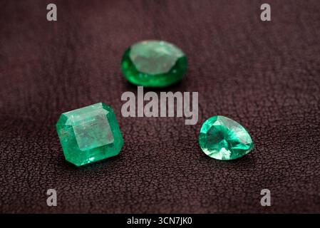 Three green gemstones are displayed on a dark surface. The stones are all different shapes and sizes, but they all have a similar color. The scene is Stock Photo