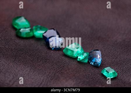 A collection of gemstones, including green and blue, are spread out on a dark surface. The stones are of various shapes and sizes, creating a visually Stock Photo