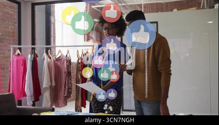 Collaborating fashion designers sketching designs at studio, with tape measure and floating icons. Creative, collaboration, industry, workspace, innov Stock Photo