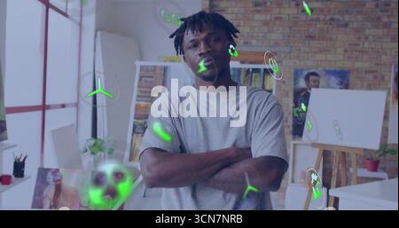 Standing man crossing arms in art studio, with easel canvas and floating green holographic icons Stock Photo