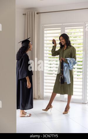 Female graduate in cap and gown receiving keys from mother in foyer, copy space Stock Photo