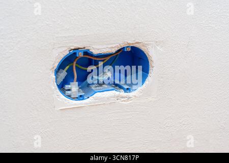 Close-up of a plastic electrical wall box with exposed wires and connectors visible in an unfinished installation during renovation, electrical work Stock Photo