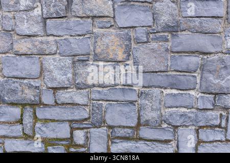 Texture of gray masonry wall made of different rectangular stones, weathering, age, and surface erosion details Stock Photo