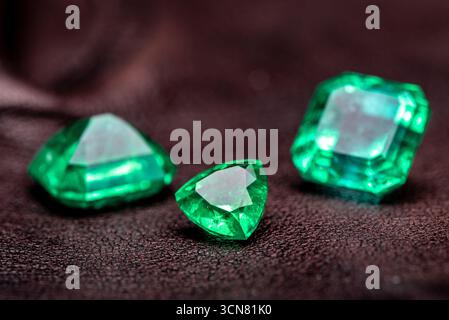 Three green gemstones are displayed on a dark surface. The stones are all different shapes and sizes, but they all have a similar color Stock Photo
