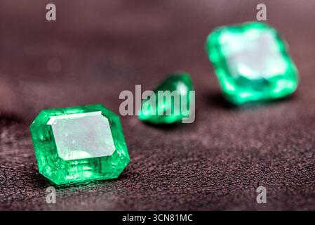 Three green gemstones are on a table. The stones are all different sizes and shapes. The table is dark brown Stock Photo