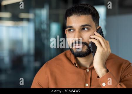 Indian businessman having a serious phone conversation, listening intently to the speaker while holding smartphone to ear in a modern office environment Stock Photo