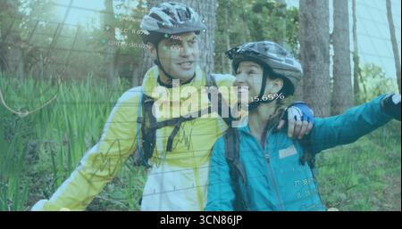 Smiling couple standing on forest path with helmets, backpacks, displaying AR data overlays Stock Photo