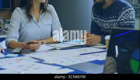 Discussing colleagues reviewing charts and taking notes at conference table, with laptop coffee cup Stock Photo