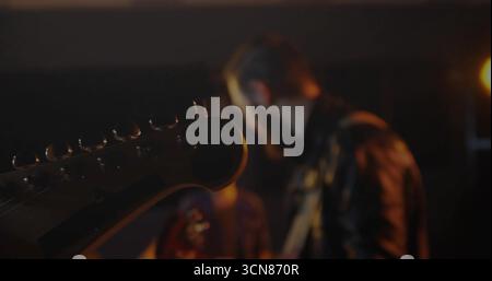 Showing electric guitar headstock with tuning pegs, strings, guitar strap on lit stage, copy space Stock Photo