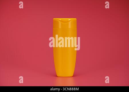 A bottle of lotion is sitting on a red background. The bottle is yellow and has a plastic cap Stock Photo