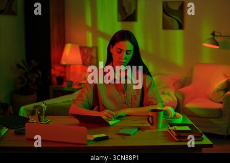 Woman Writing Notes at Desk in Home Office at Night Stock Photo
