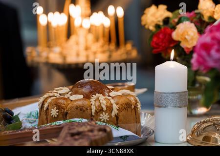 Beautifully arranged Orthodox Easter table featuring a decorated Paska bread loaf, lit candles creating a warm golden glow, and a vibrant bouquet of f Stock Photo