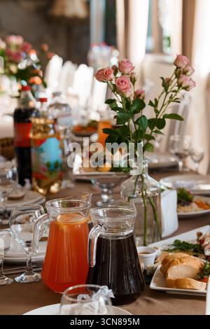 A beautifully arranged wedding table showcases delicate pink roses, crystal glassware filled with various beverages, and plates with appetizers, refle Stock Photo
